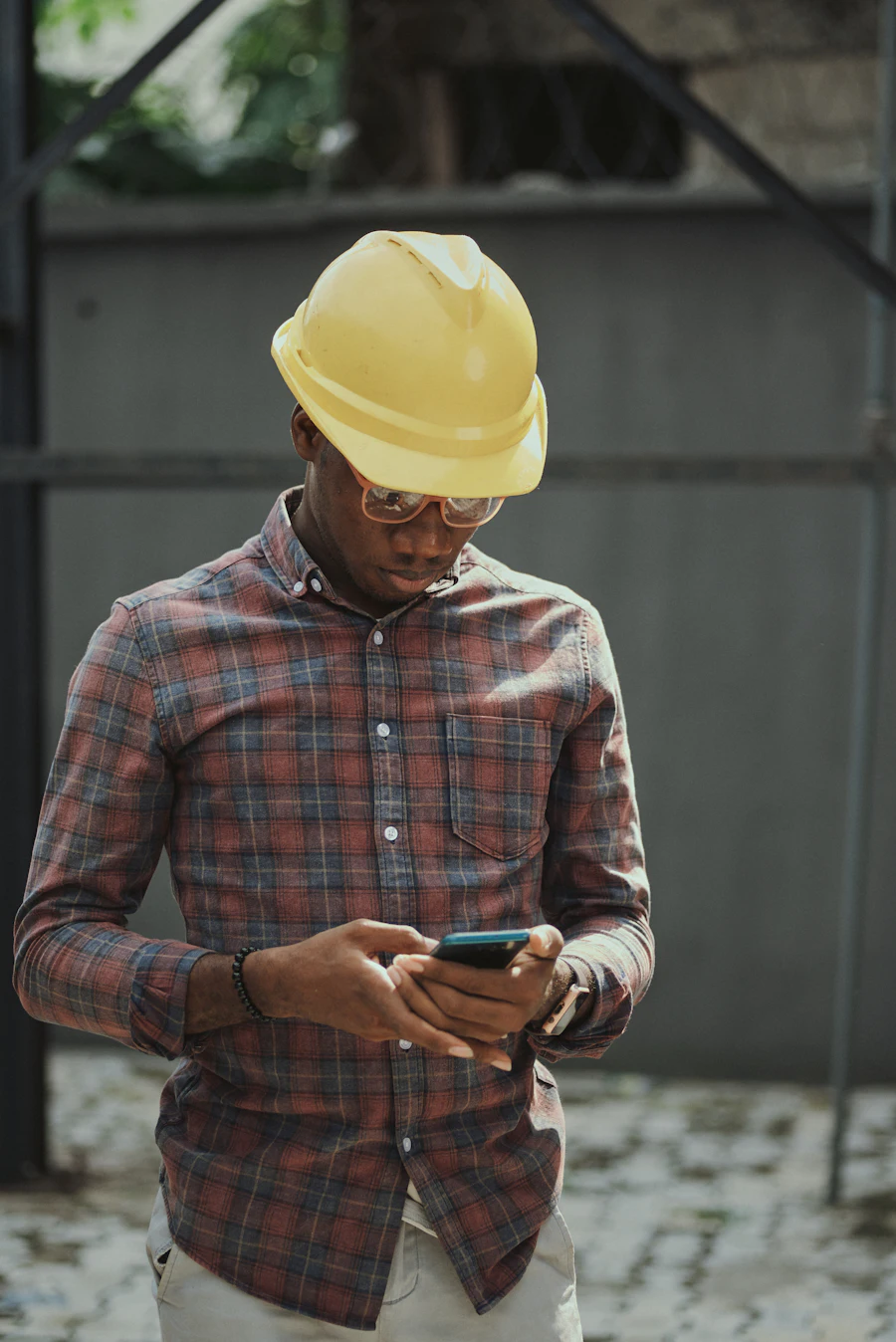Site engineer in a yellow hard hat checking a phone