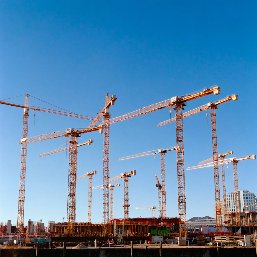 A row of tower cranes over a large building site under a blue sky