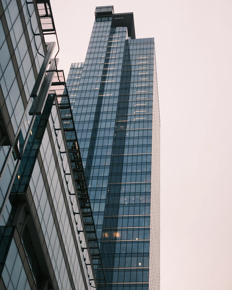 Dark glass office tower photographed from below against a pale pink sky