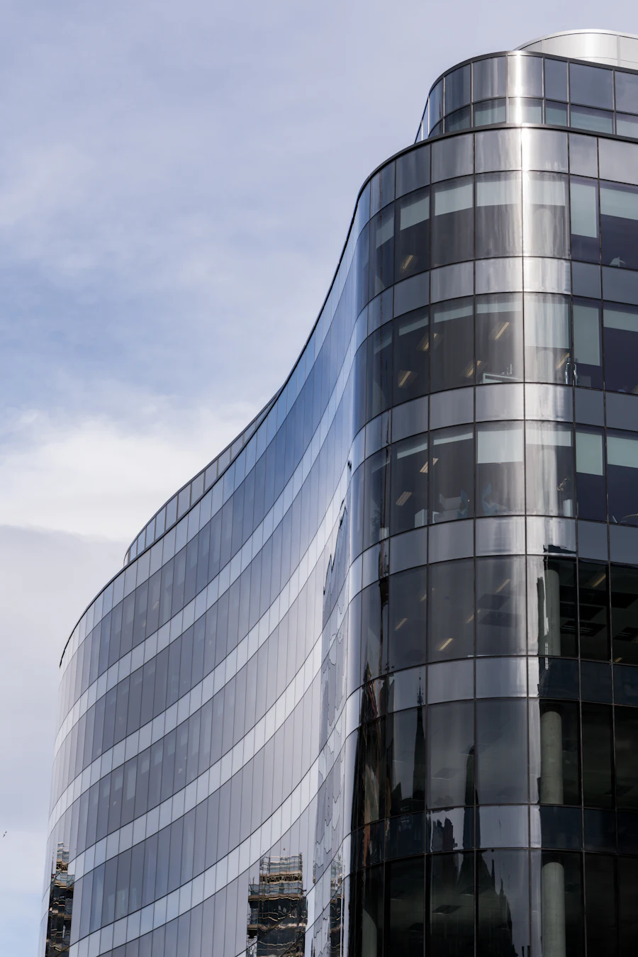 Curved glass office building reflecting a blue sky